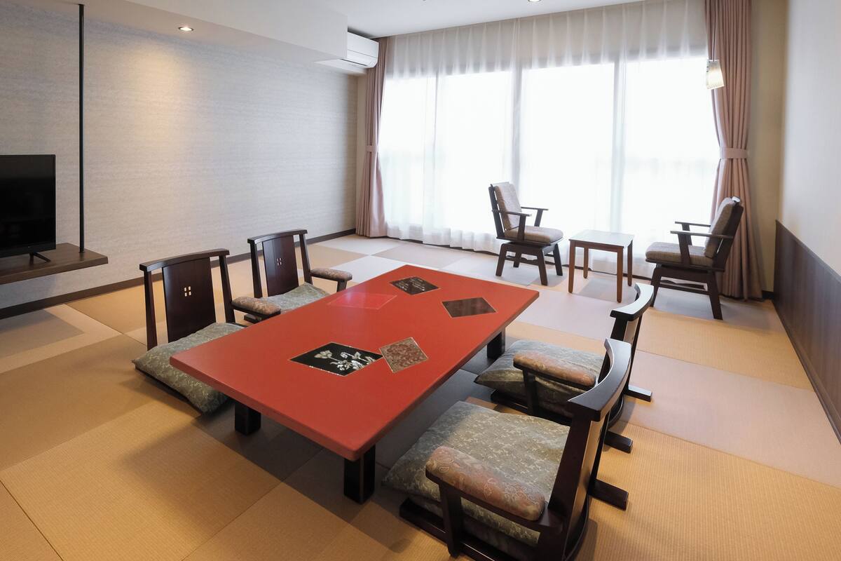 Une chambre d’hôtel moderne dotée d’un grand téléviseur à écran plat, d’une table de conférence rouge, de tatamis et de meubles japonais traditionnels.