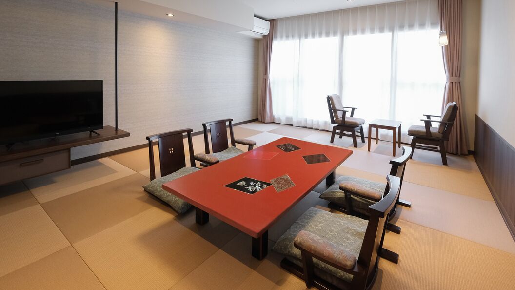 A modern hotel room with a large TV, a red dining table, and traditional Japanese tatami mats.