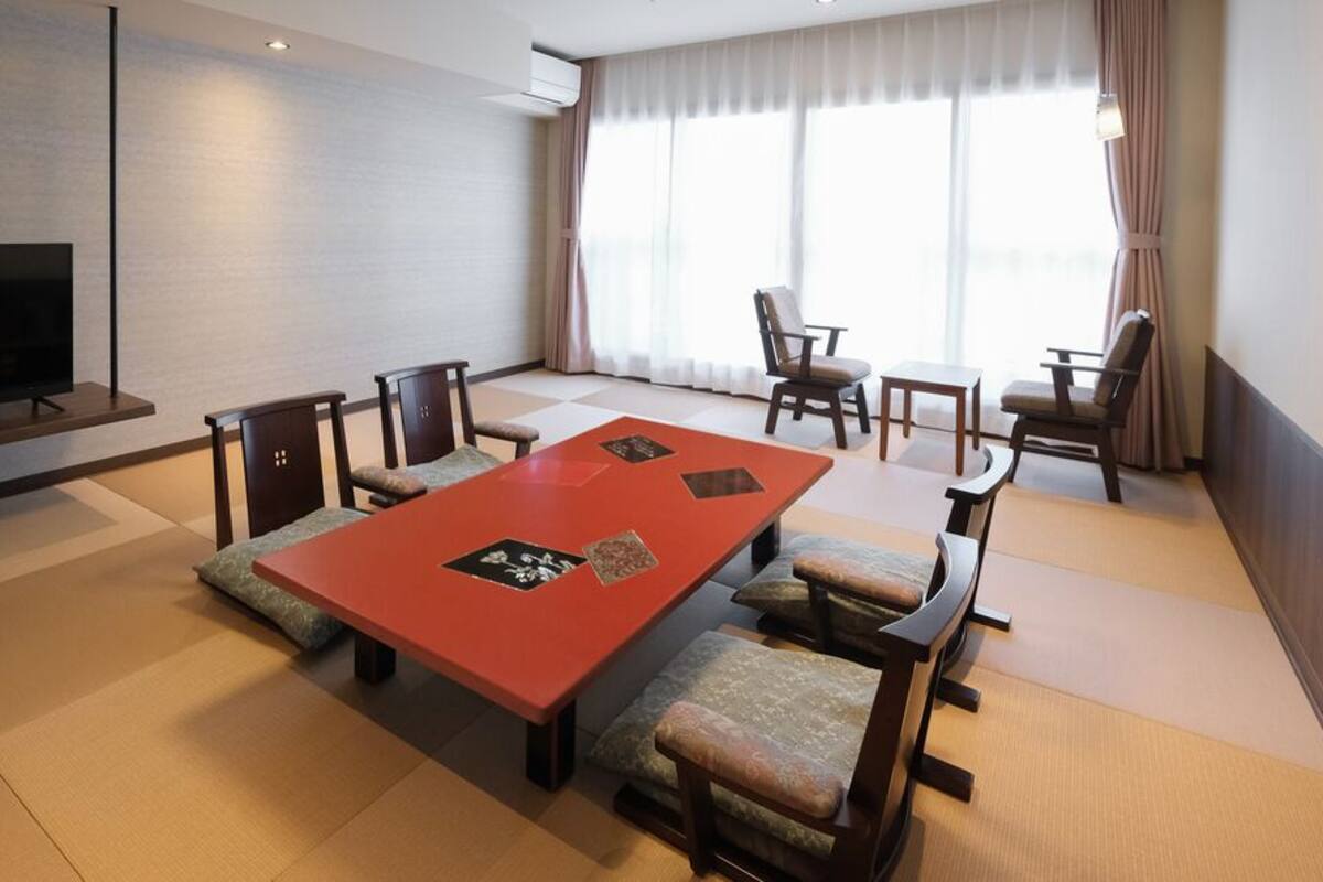 Une chambre d’hôtel moderne dotée d’un grand téléviseur, d’une table à manger rouge et de tatamis japonais traditionnels.