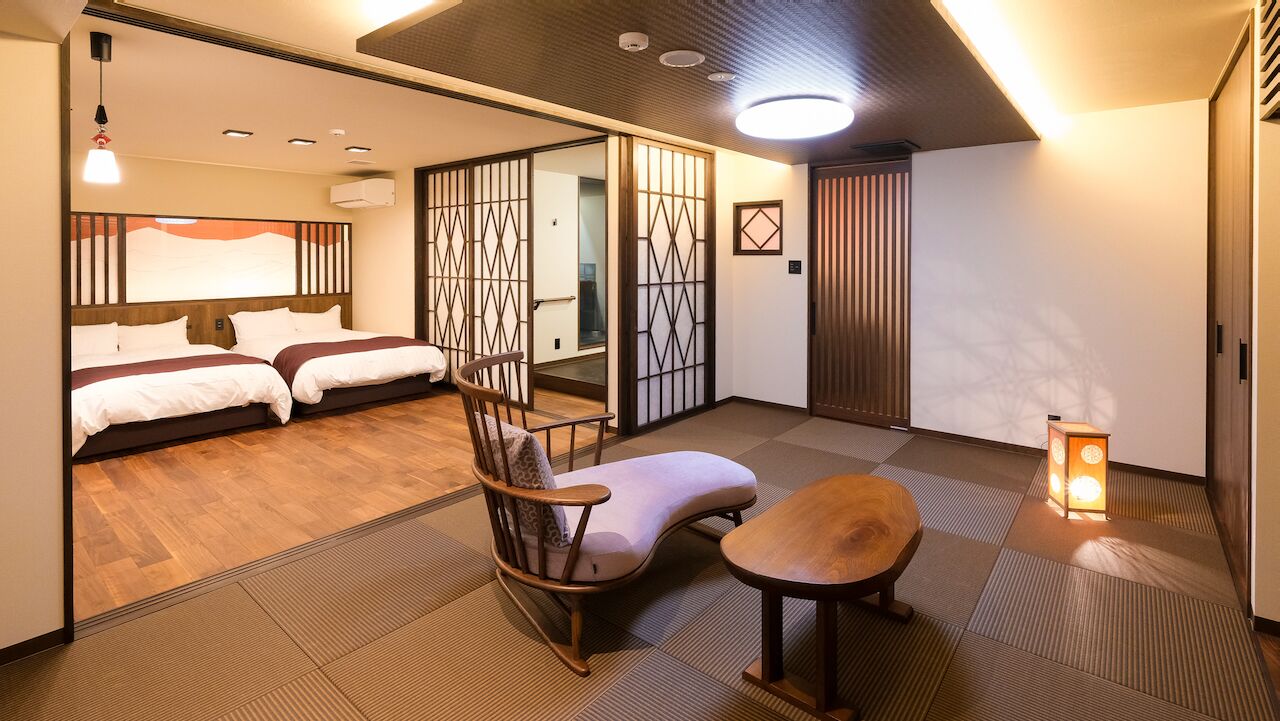 A room with a bed, a chair, a table, and a sliding door.