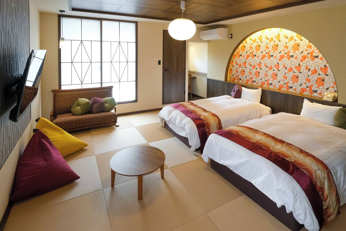 Une chambre d’hôtel avec deux lits, un canapé, une petite table et une grande fenêtre.