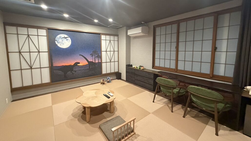 A traditional Japanese-style room with tatami flooring, a low table, green cushioned chairs, and a large window with shoji screens.