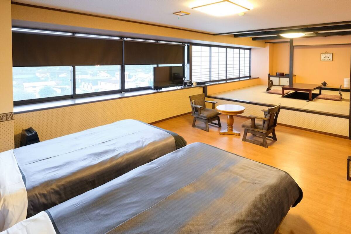 Une chambre d’hôtel avec deux lits, une petite table, des chaises, un téléviseur et une grande fenêtre.