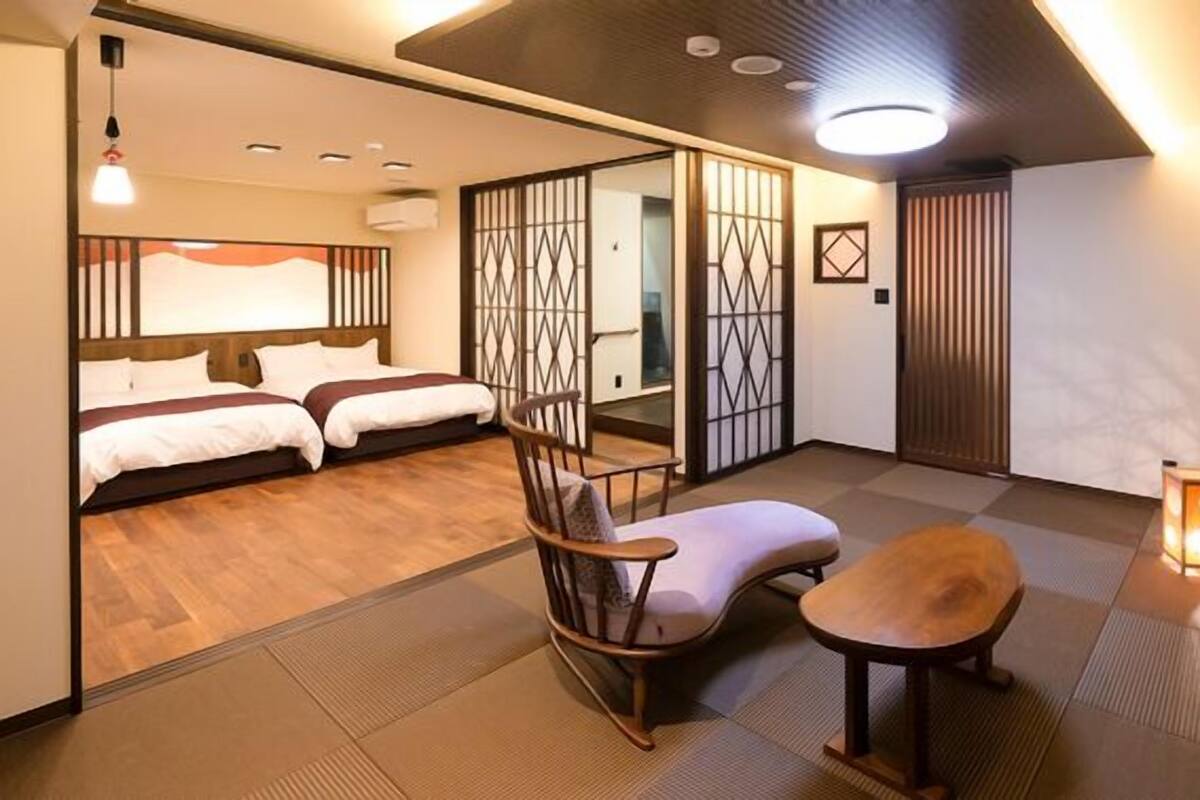 Une pièce de style japonais traditionnel, avec un sol recouvert de tatamis, un futon servant de lit, une petite table en bois, un fauteuil rembourré et des paravents coulissants en papier de riz (shoji).