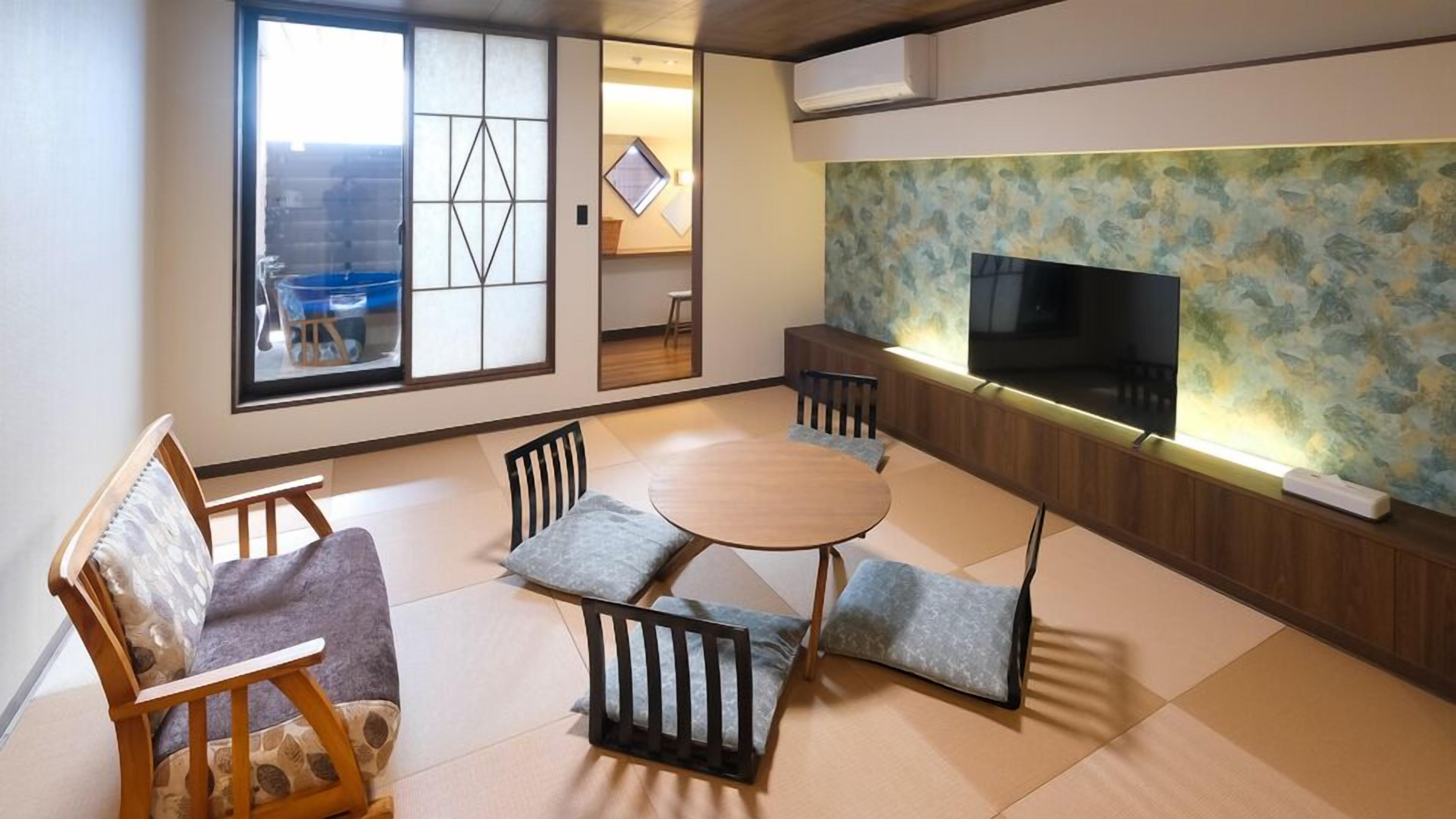 A traditional Japanese-style living room with tatami flooring, a low table, and a television mounted on a wooden panel wall.