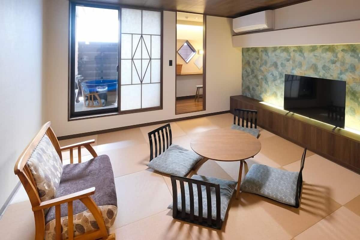 Un salon de style japonais traditionnel, avec un sol recouvert de tatamis, une table basse et un téléviseur fixé sur un mur en panneaux de bois.