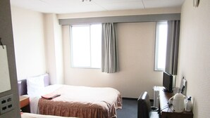 Ein Hotelzimmer mit zwei Betten, einem Schreibtisch, einem Sessel, einem Fernseher und einem Fenster mit Vorhängen.