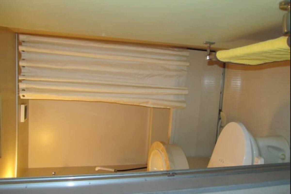 Une petite salle de bain fermée, équipée de toilettes et d’une fenêtre avec des stores.