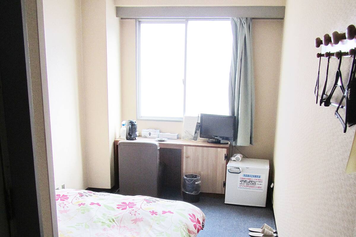 Une chambre d’hôtel avec un lit, un bureau équipé d’un ordinateur, une fenêtre et un porte-manteau fixé au mur.