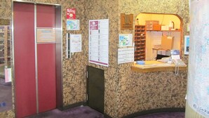 Ein Hotel-Empfangsbereich mit einer roten Tür, einem Bulletin Board mit verschiedenen Aushängen, einer kleinen Rezeption und einer Karte an der Wand.