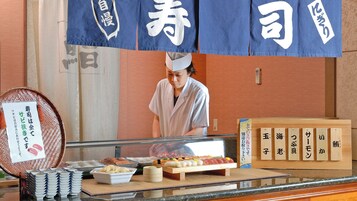 Un bar de sushi con diversos tipos de sushi expuestos en una tabla de madera, una selección de palillos y un cartel con texto japonés.