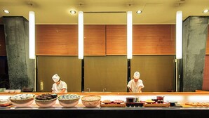 A sushi bar with chefs preparing food, a counter with various dishes, and a modern interior with wooden panels and pendant lights. - Kominato Miiri Onsen Hotel Green Plaza Kamogawa (Kamogawa)