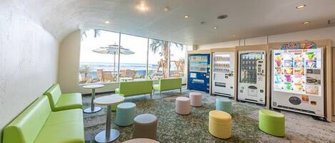A room with green seating, vending machines, and a view of the ocean.