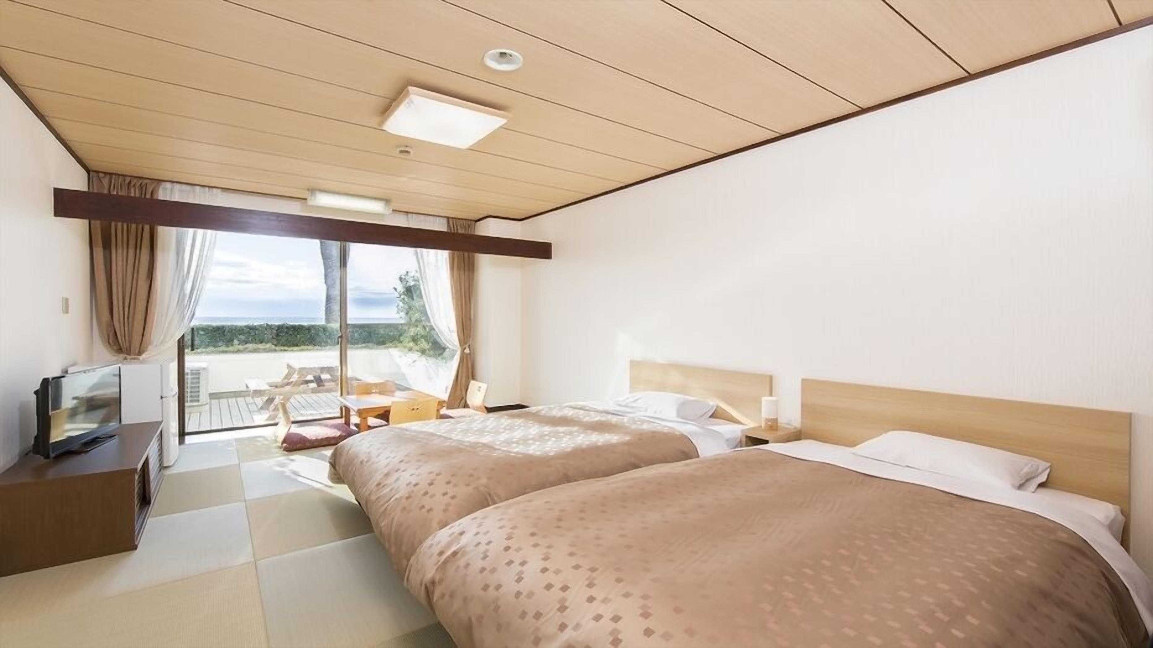 A hotel room with two beds, a desk, a chair, and a view of the beach.