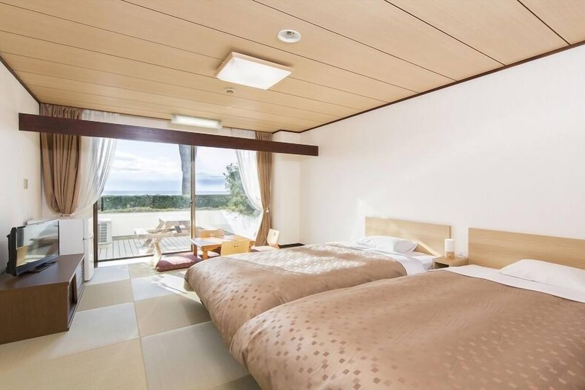 A hotel room with two beds, a desk, a chair, and a view of the beach.