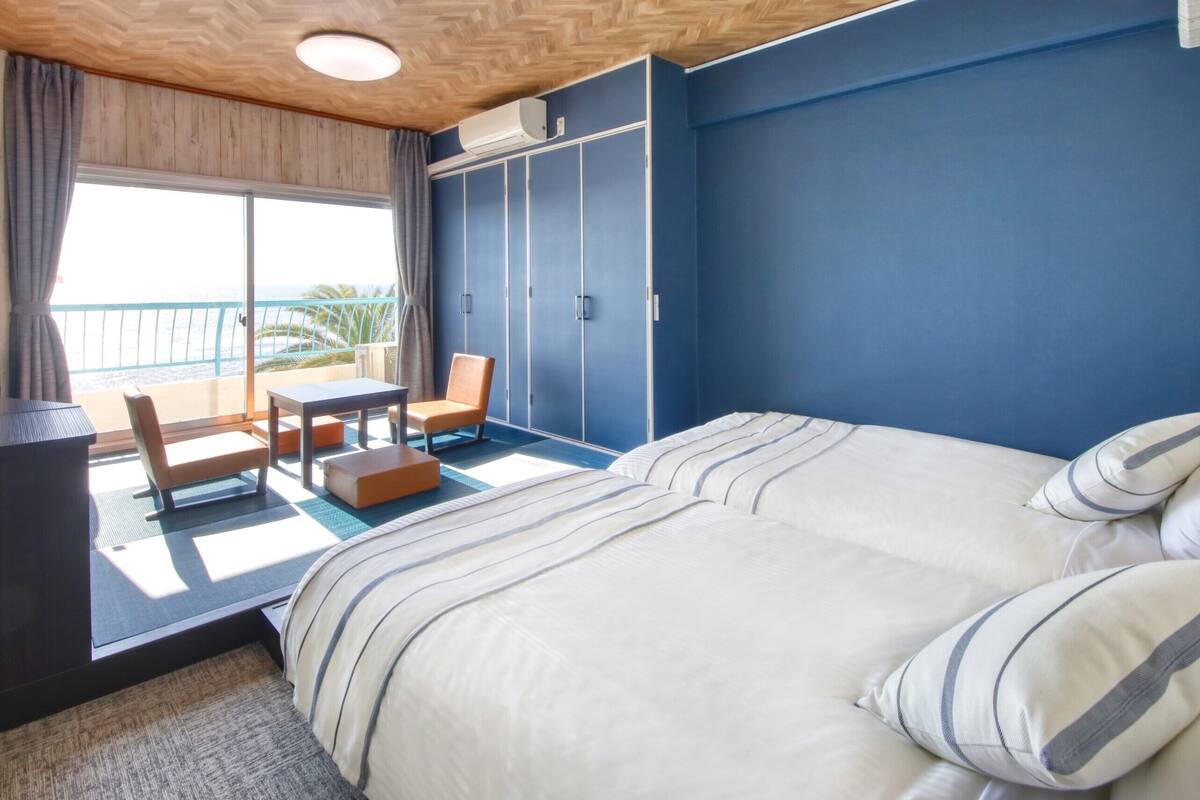 A hotel room with a bed, a chair, a table, and a view of the ocean.