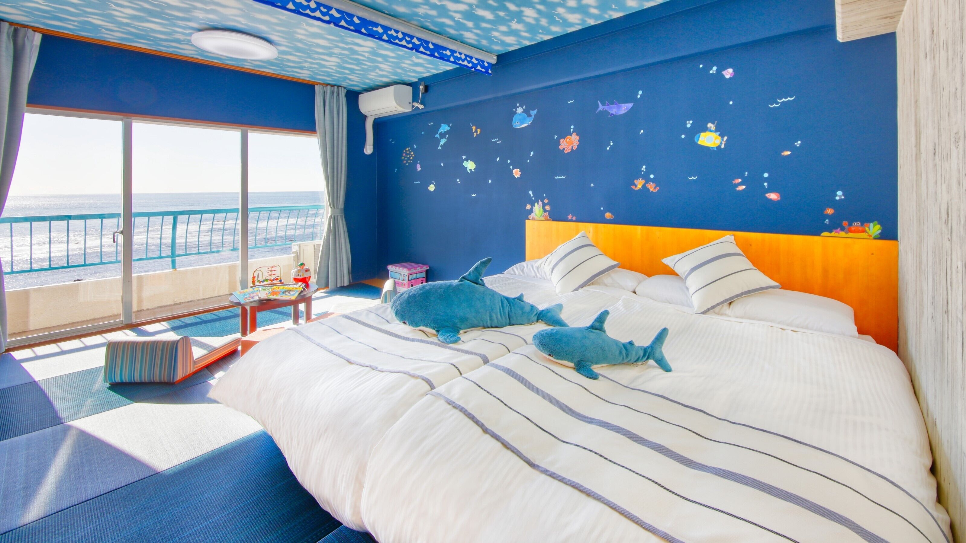 A bedroom with a bed, pillows, a nightstand, a window with a view of the sea, and a ceiling with a wave pattern.