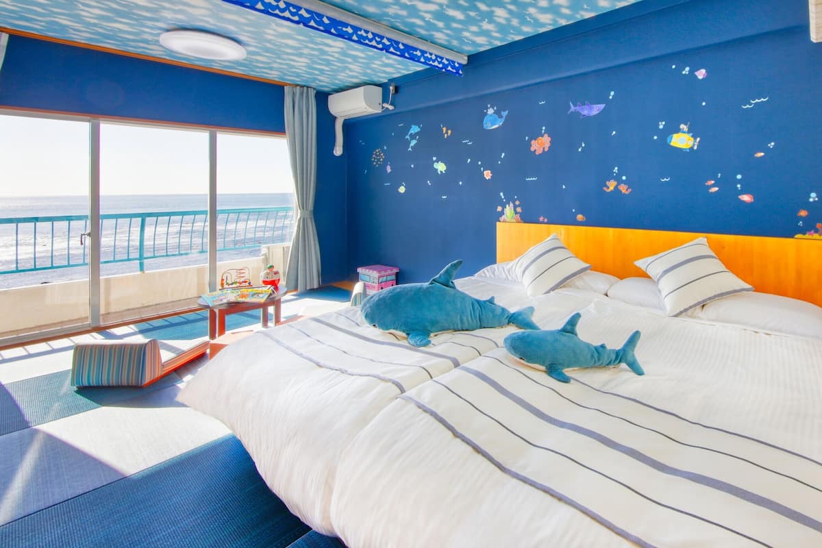 A bedroom with a bed, pillows, a nightstand, a window with a view of the sea, and a ceiling with a wave pattern.