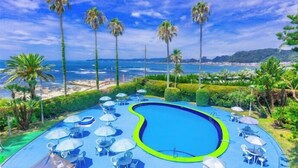 A pool with lounge chairs and umbrellas, surrounded by palm trees and a view of the ocean. - Kominato Miiri Onsen Hotel Green Plaza Kamogawa (Kamogawa)