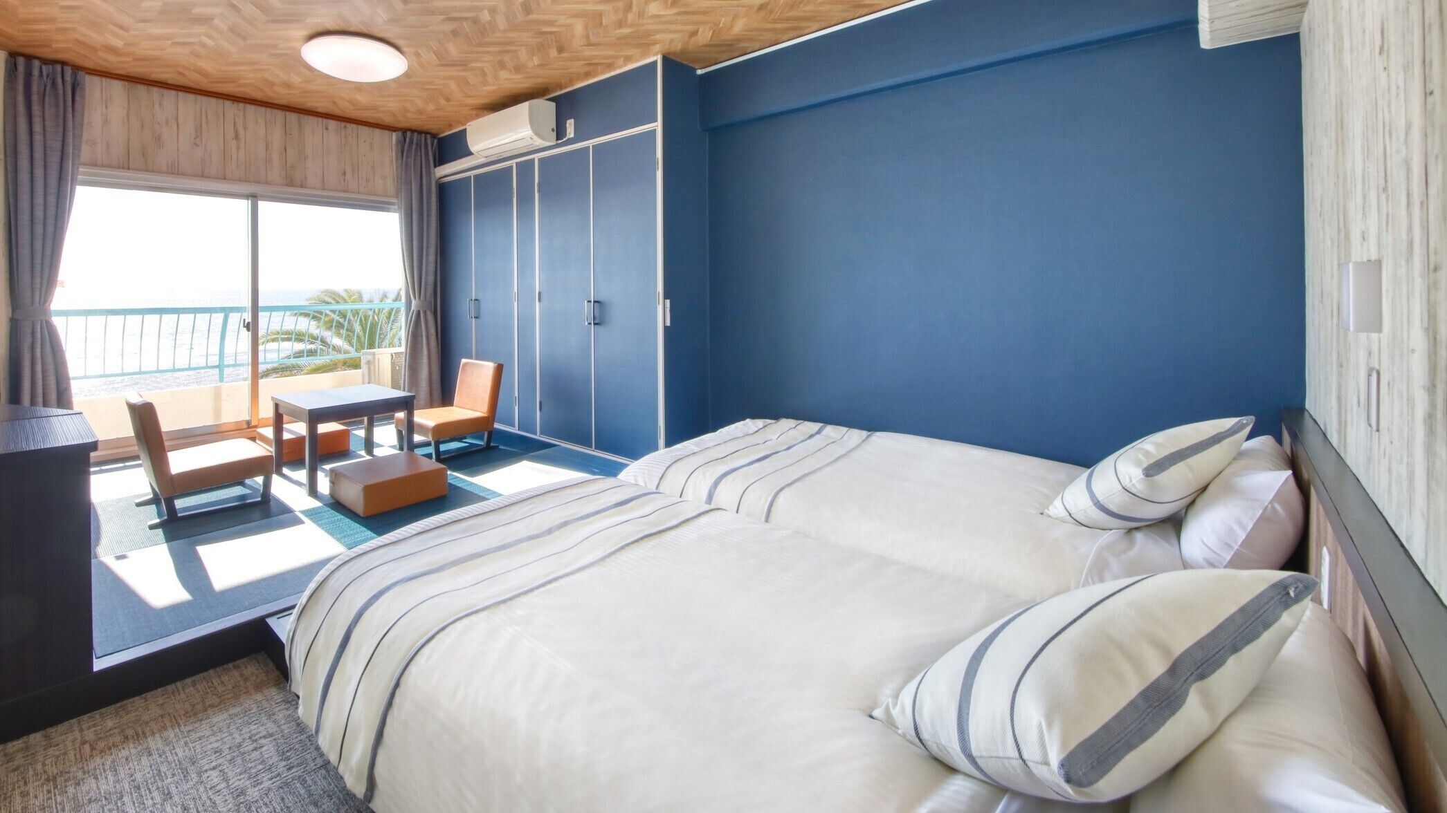 A hotel room with a bed, a chair, a small table, and a balcony with a view.