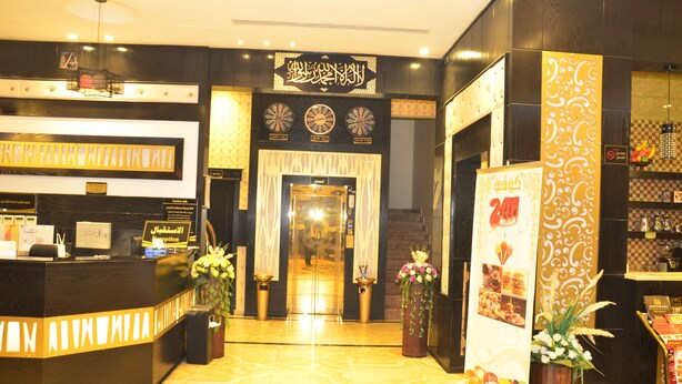 A hotel reception area with a reception desk, a mirror, and a sign with Arabic script. - Zahrat Rozah (Riyadh)