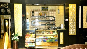 A coffee shop with a checkered wall pattern, a coffee machine, and a display case with snacks and drinks. - Zahrat Rozah (Riyadh)