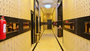 A hotel hallway with patterned wallpaper, a chandelier, a fire extinguisher, and a reception desk. - Zahrat Rozah (Riyadh)