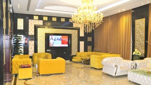A luxurious lobby with a large TV screen, plush yellow and white sofas, a grand chandelier, and a decorative wall with intricate patterns. - Zahrat Rozah (Riyadh)