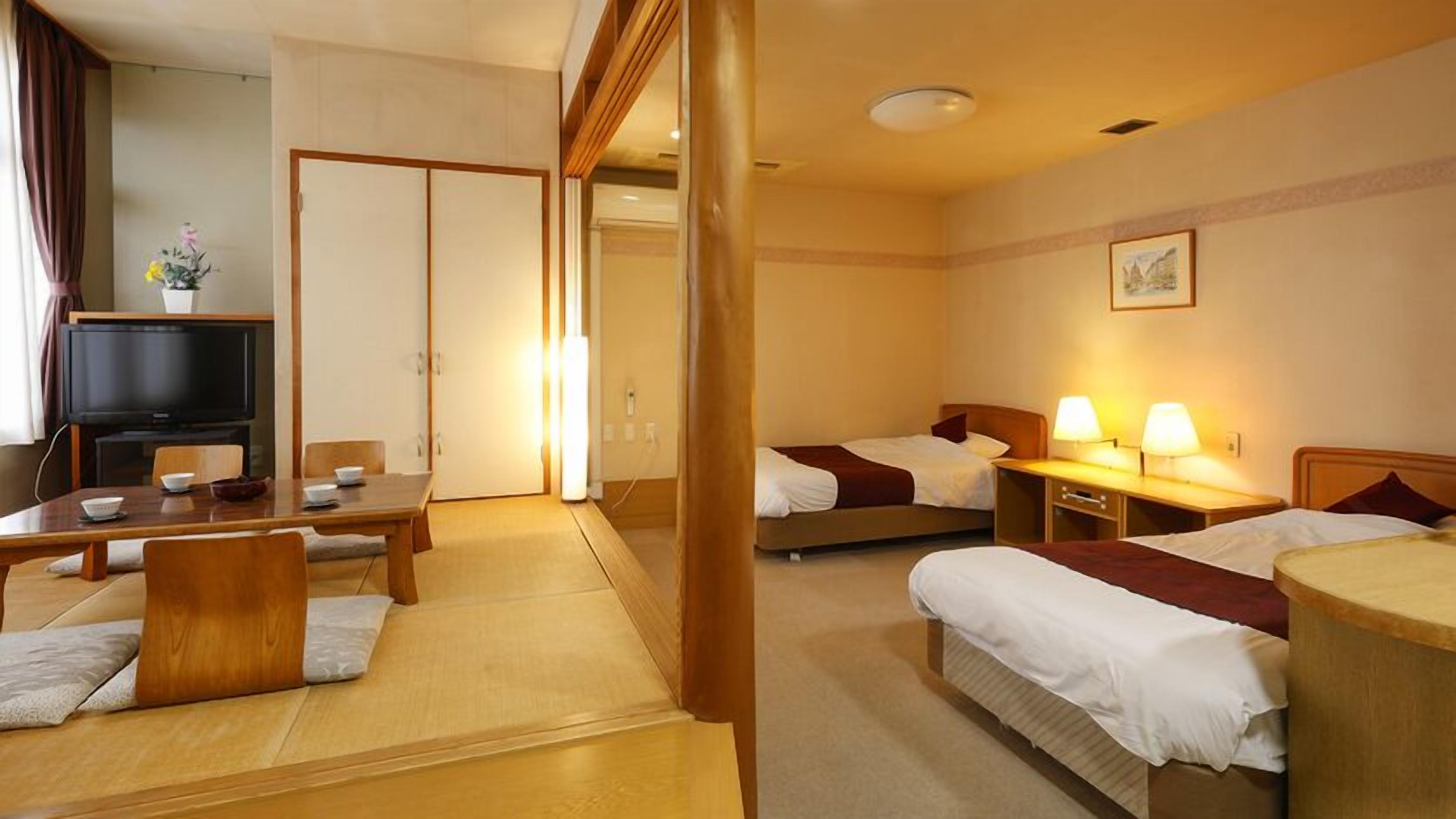 Habitación de hotel con comedor, dos camas, televisor y un cuadro en la pared.