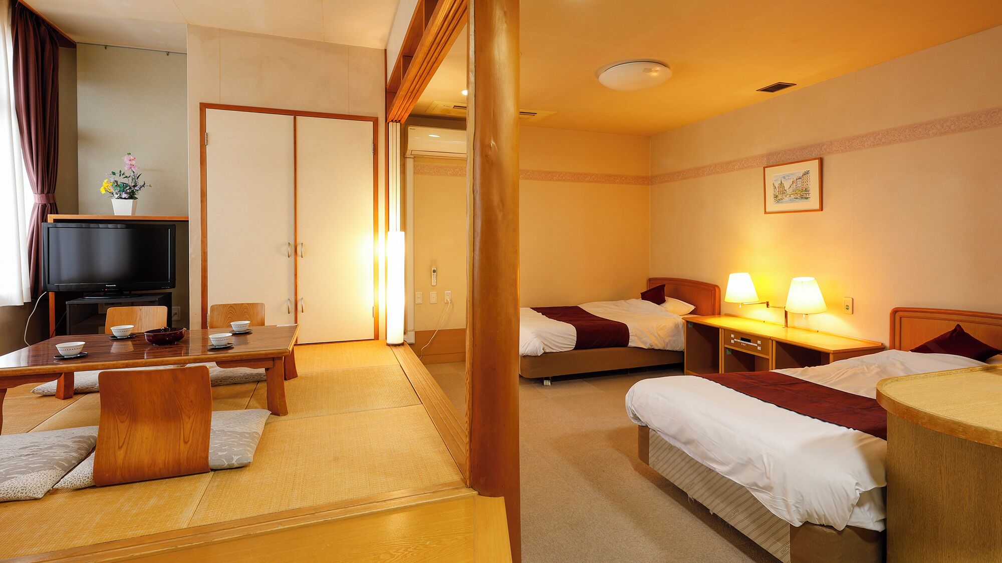 Una habitación de hotel con cama, mesitas de noche, televisor y un rincón de comedor con mesa y sillas.