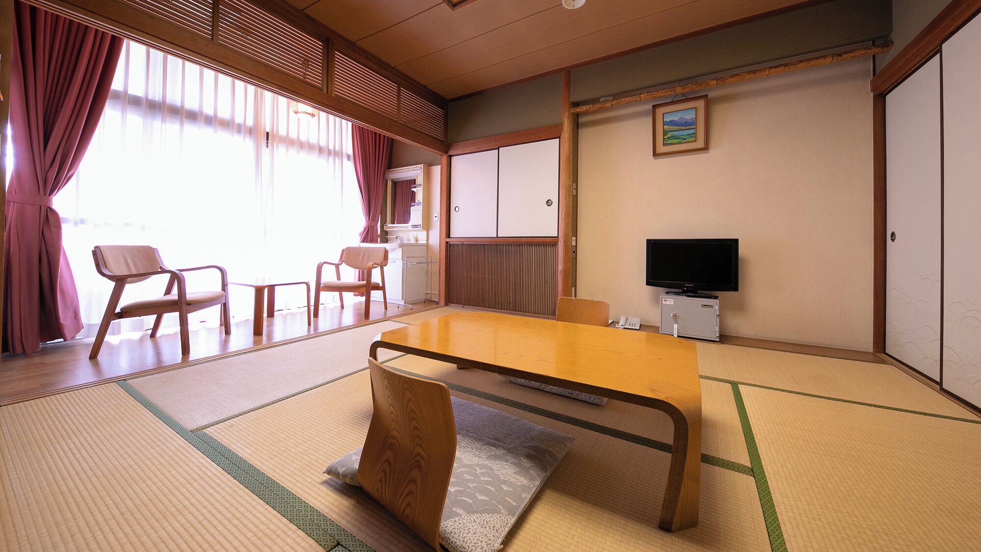 Una habitación japonesa tradicional con suelo de tatami, una mesa baja, sillas, un televisor y puertas correderas.