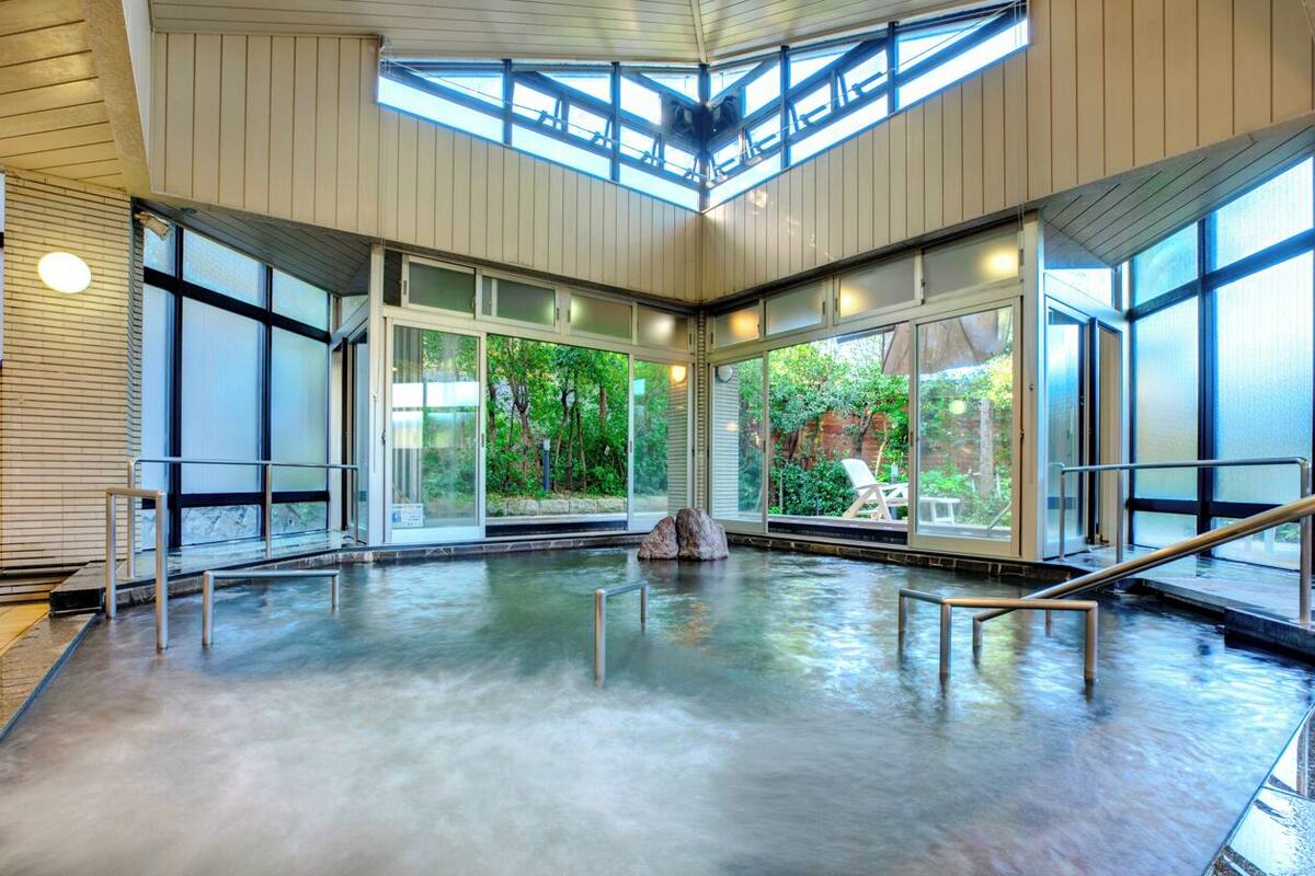 Une piscine intérieure avec des parois en verre transparent, une verrière et un élément décoratif en pierre au centre.