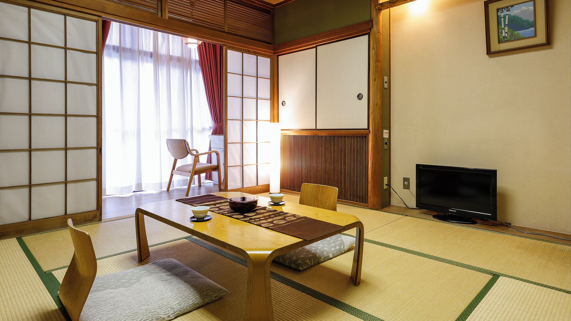 Una habitación tradicional japonesa con suelo de tatami, una mesa baja, un televisor y puertas correderas.