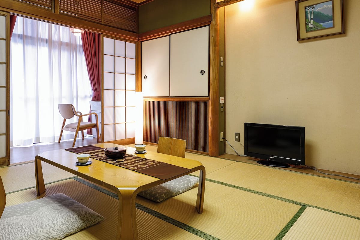 Une pièce de style japonais traditionnel, avec un sol recouvert de tatamis, une table basse, un téléviseur et des portes coulissantes.