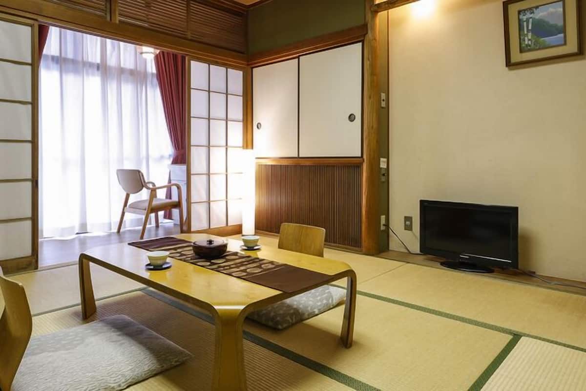 Une pièce de style japonais traditionnel, avec un sol recouvert de tatamis, une table basse avec des coussins, un téléviseur et des portes coulissantes.