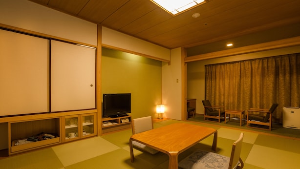 Uma sala de estar tradicional japonesa com tatames, uma mesa de madeira baixa e uma televisão.