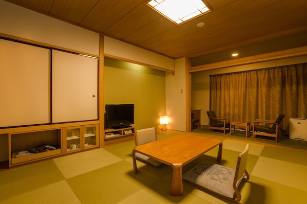 Ett traditionellt japanskt vardagsrum med tatamimattor på golvet, ett lågt träbord och en tv.