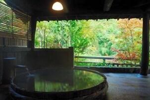 Un onsen japonés tradicional con una bañera de madera, persianas de bambú y vistas a un exuberante jardín.