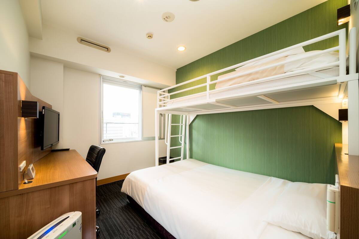 Una habitación de hotel con una cama litera, un escritorio con ordenador y una televisión.