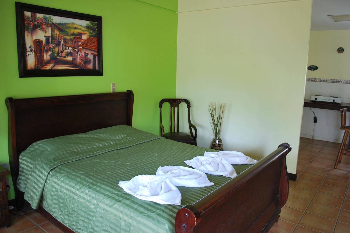 A bed with a green bedspread and two towels folded on it.