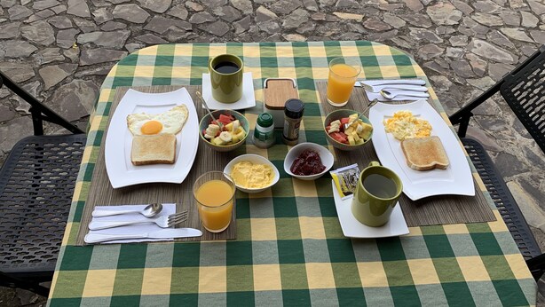 A checkered table set outdoors with breakfast items including toast, eggs, fruit, and beverages. - Dos Palmas Studio Apartments (Rio Segundo)