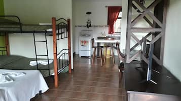 A dormitory room with bunk beds, a kitchenette, and a desk area.