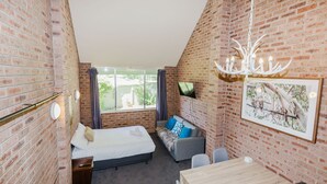 Ein Zimmer mit Backsteinwand, einem Bett, einem Schreibtisch, einem Stuhl, einem Fernseher und einer Kristallleuchter.