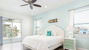 Quarto com cama, mesa de cabeceira, ventilador de teto e janela com persianas.