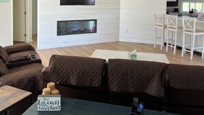 A modern living room with a fireplace, a television, and a kitchen area labeled "BEACH HOUSE". - Ocean Beach/Corneille Est, Fire Island Beach House (Ocean Beach (Cornielle Estates))