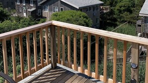 A wooden deck with a railing overlooking a residential area and a beach. - Ocean Beach/Corneille Est, Fire Island Beach House (Ocean Beach (Cornielle Estates))