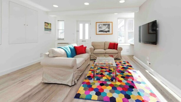 A spacious living room with a large window, a beige sofa, a colorful hexagonal rug, and a flat-screen TV mounted on the wall. - Notting Hill Chic sleeps 4-5 - 2 bedrms/2 bathrms-one en-suite + single SofaBed (London)