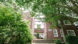 Un bâtiment traditionnel en briques, doté d’une entrée centrale et entouré d’une végétation luxuriante et d’arbres.