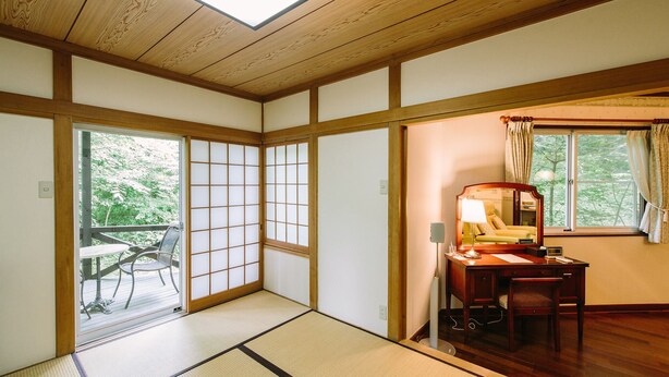 Une pièce de style japonais traditionnel, avec un sol recouvert de tatamis, une porte coulissante de type shoji, un bureau en bois et une vue sur la verdure à l’extérieur.