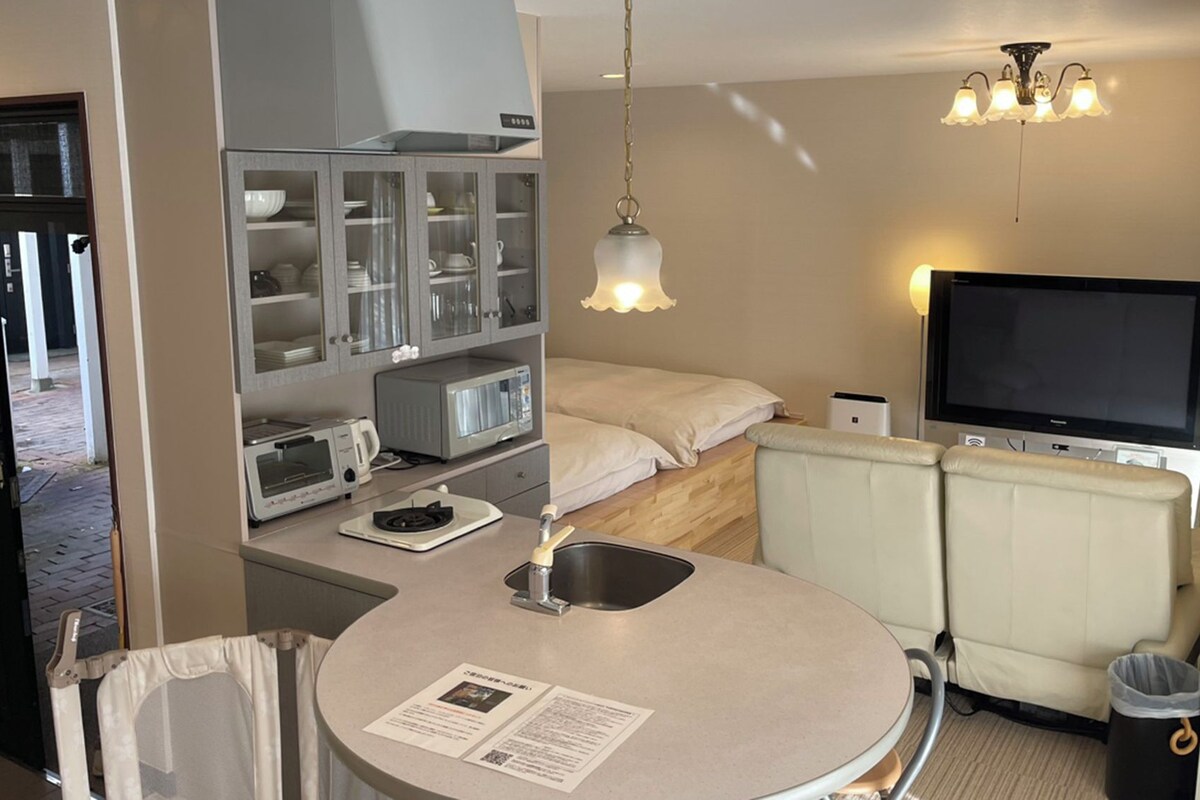 A compact hotel room with a kitchenette, a bed, a TV, and a small dining area.